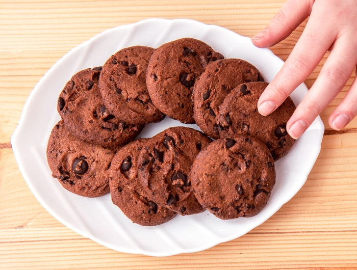 hand reaching over white plate full of chocolate cookies